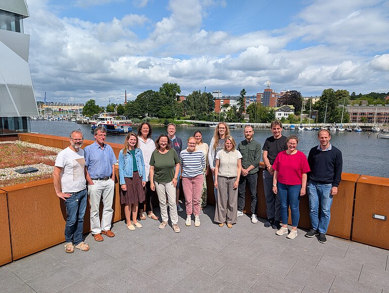Eine Gruppe Menschen steht bei Sonnenschein auf der Dachterrasse
