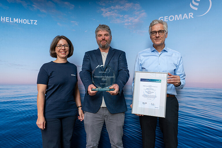 Eine Frau und zwei Männer vor einem Hintergrund, der Meer zeigt