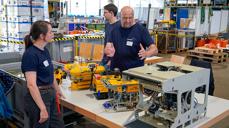 Small models of underwater vehicles on a table, with two men behind them and a woman in front of them