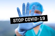 Der Schriftzug "Stop Covid-19" vor einem Menschen mit Maske