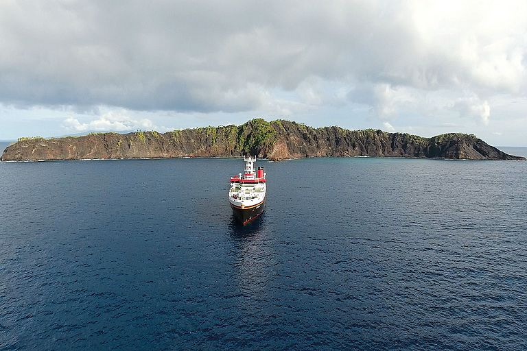 Das Forschungsschiff SONNE liegt vor einer schmalen Insel aus Vulkangestein. 